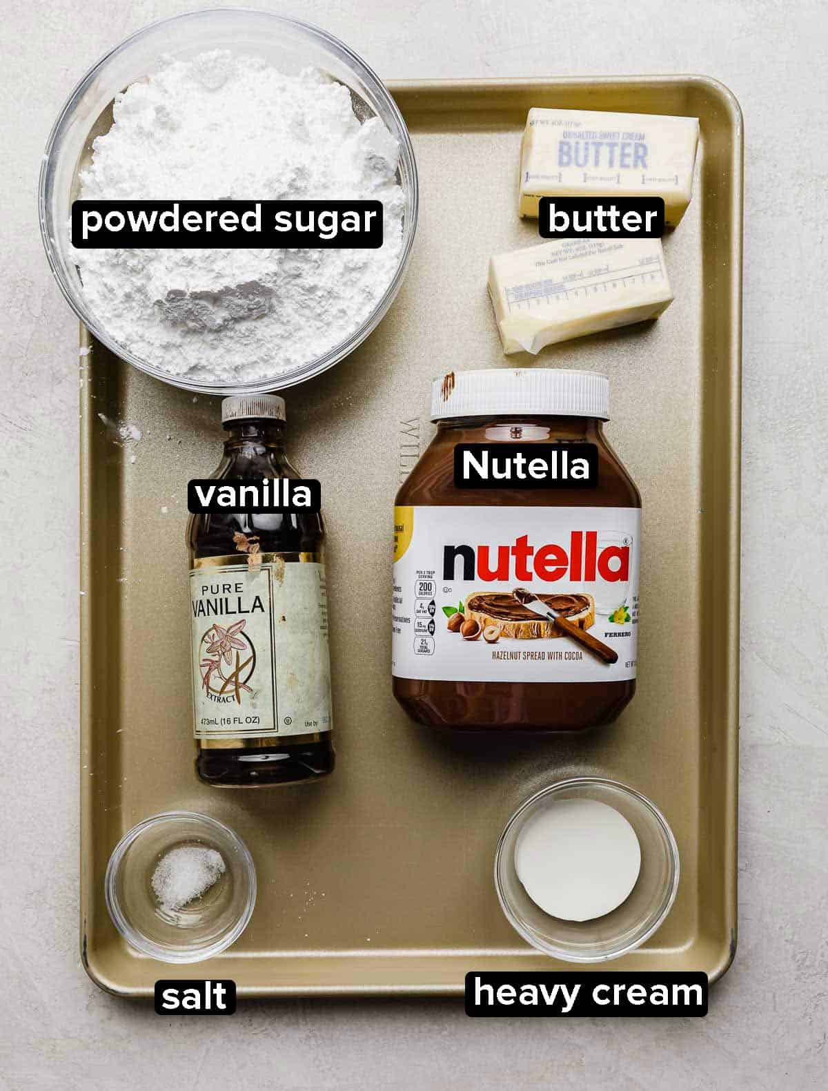 Nutella Frosting ingredients on a gold baking sheet: powdered sugar, Nutella hazelnut spread, heavy cream, butter, vanilla, and salt. 