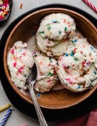 Three scoops of Birthday Cake Ice Cream with sprinkles, in a brown bowl.