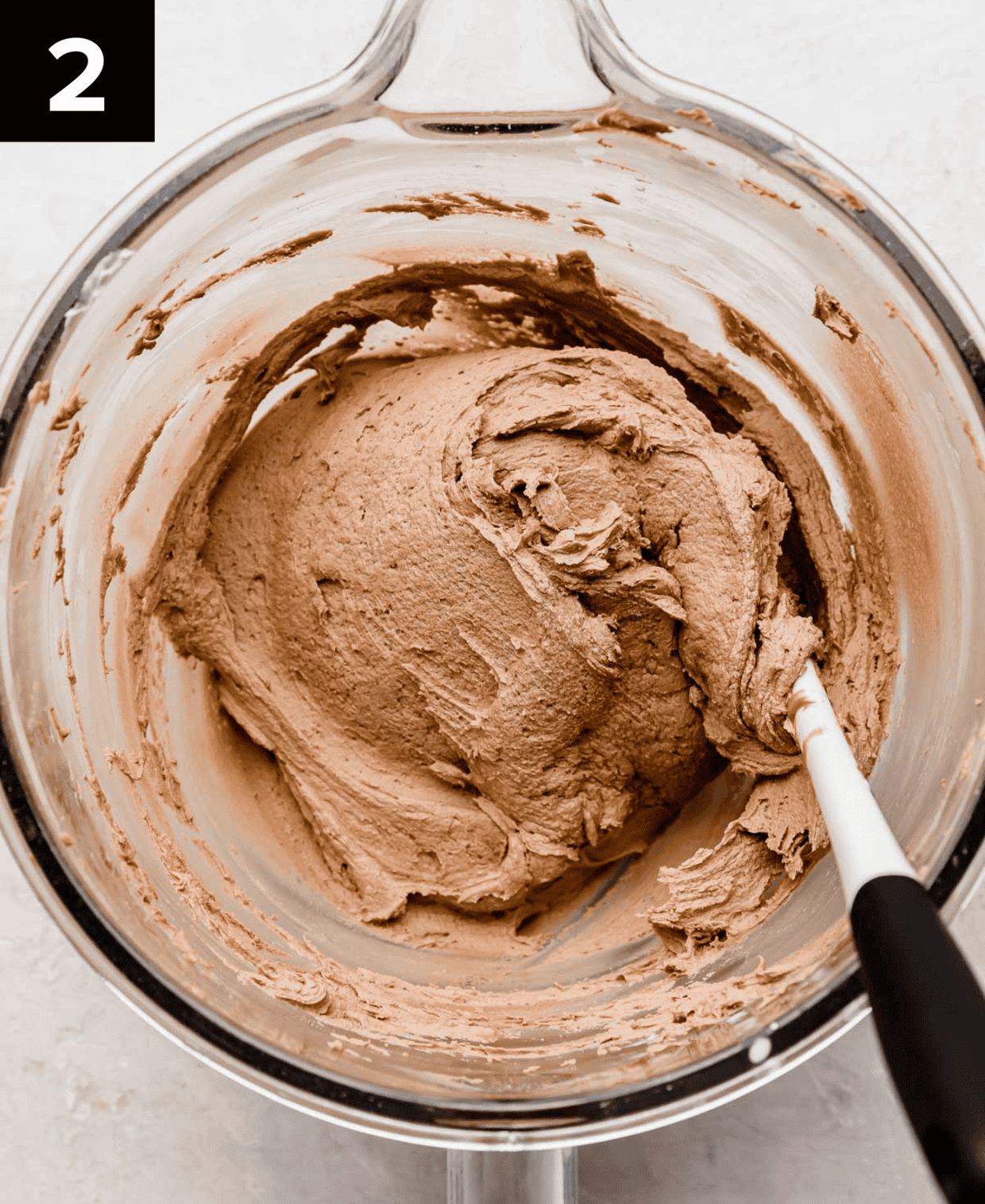 Nutella buttercream frosting in a glass mixing bowl on a light gray background.