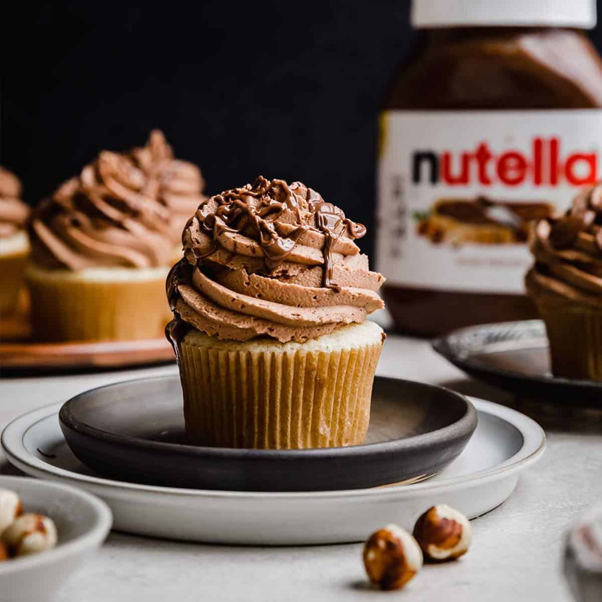 A Nutella Cupcake on a black plate with a Nutella jar in the background.