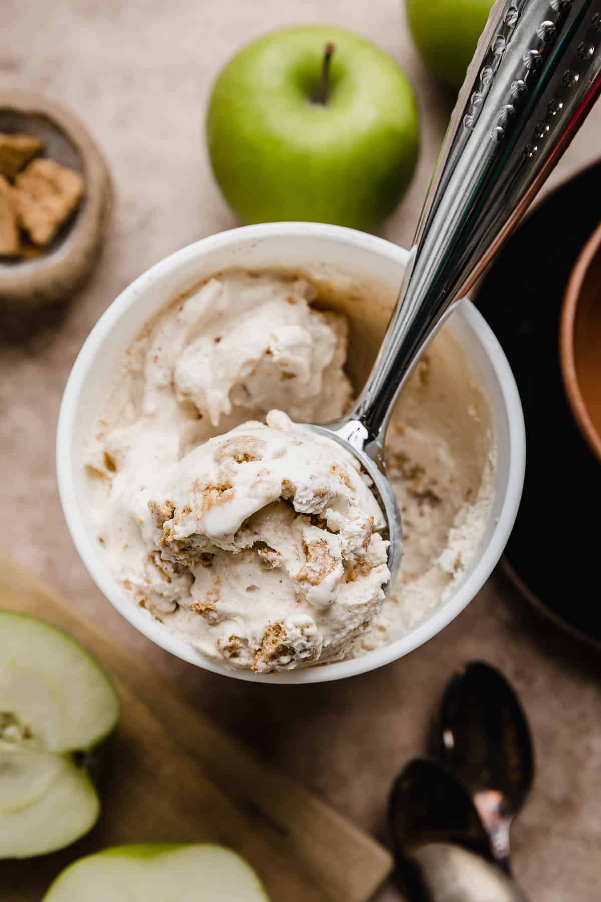 An ice cream scoop filled with homemade Apple Pie Ice Cream with Granny Smith apples in the background.