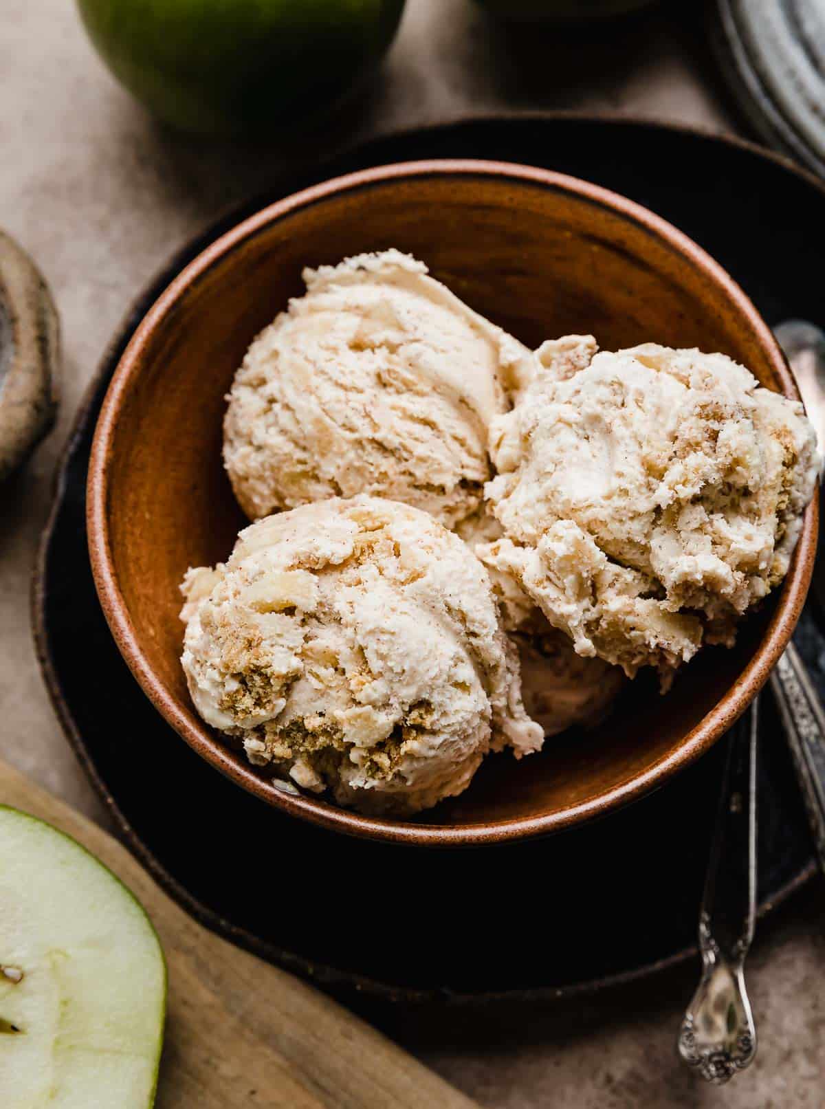 Three scoops of Apple Pie Ice Cream studded with cinnamon apples and cinnamon graham cracker pieces in a brown bowl.