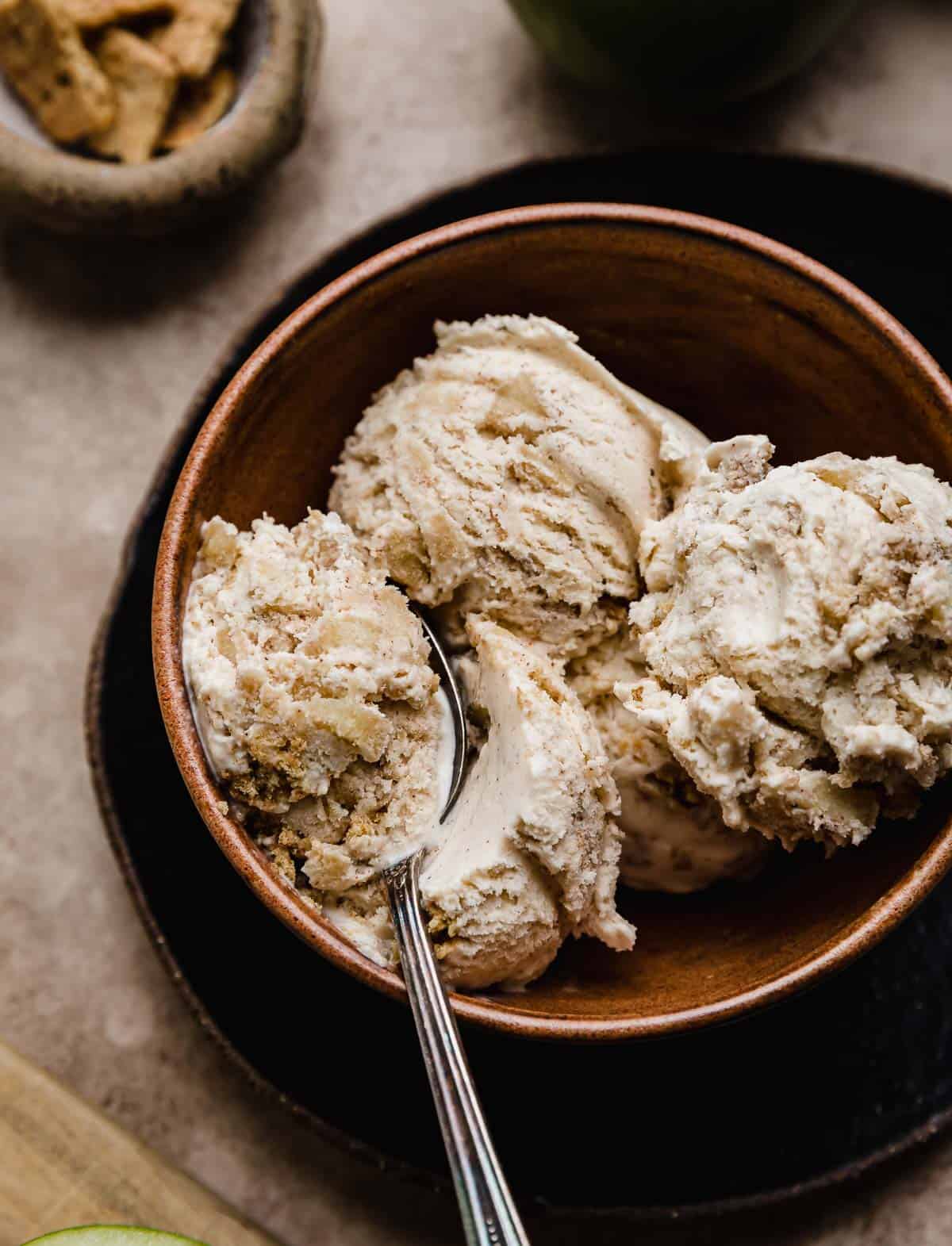 A spoon scooping out Apple Pie Ice Cream from a brown bowl.