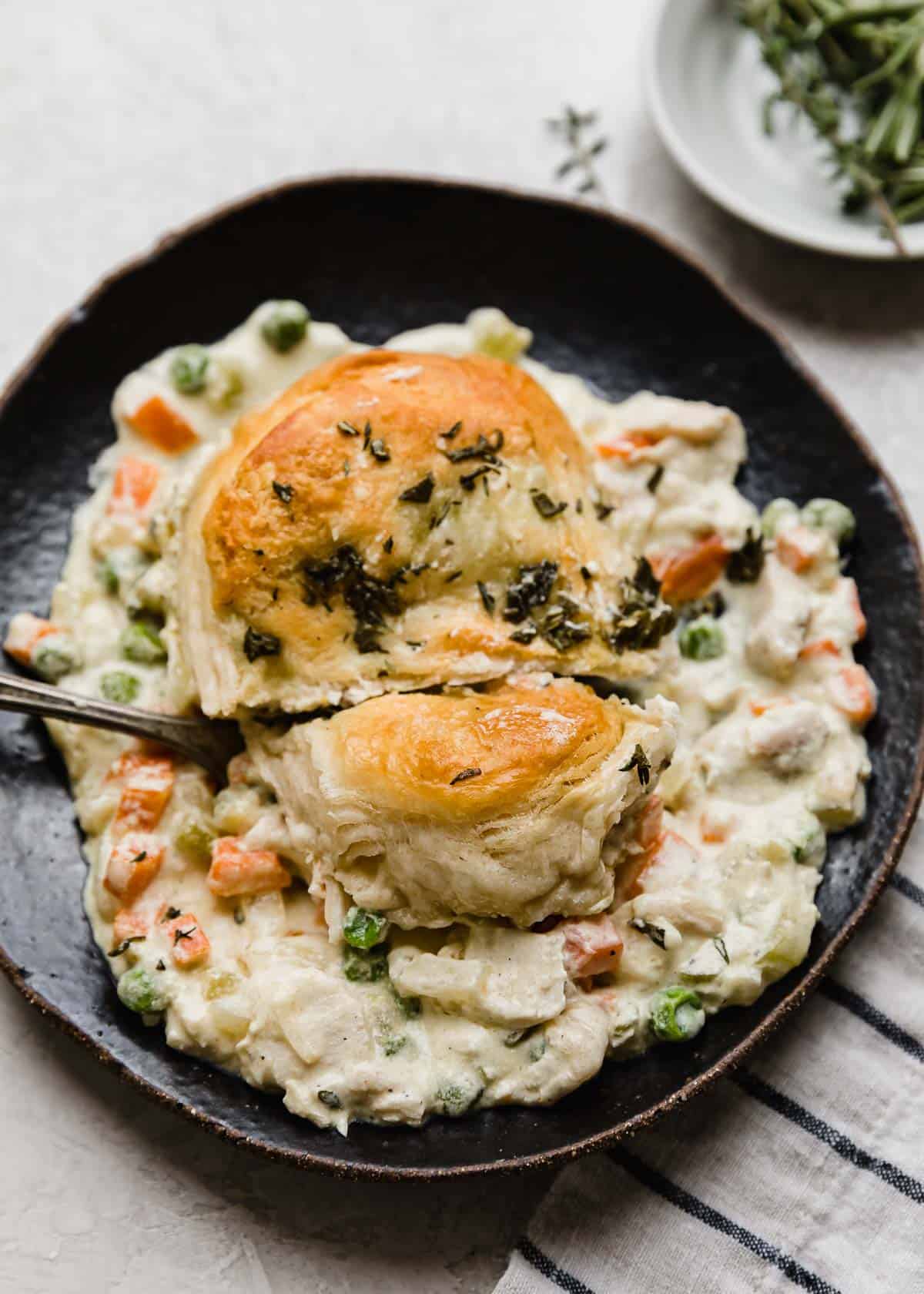 A biscuit and chicken pot pie mixture on a black plate with a fork cutting into the biscuit.