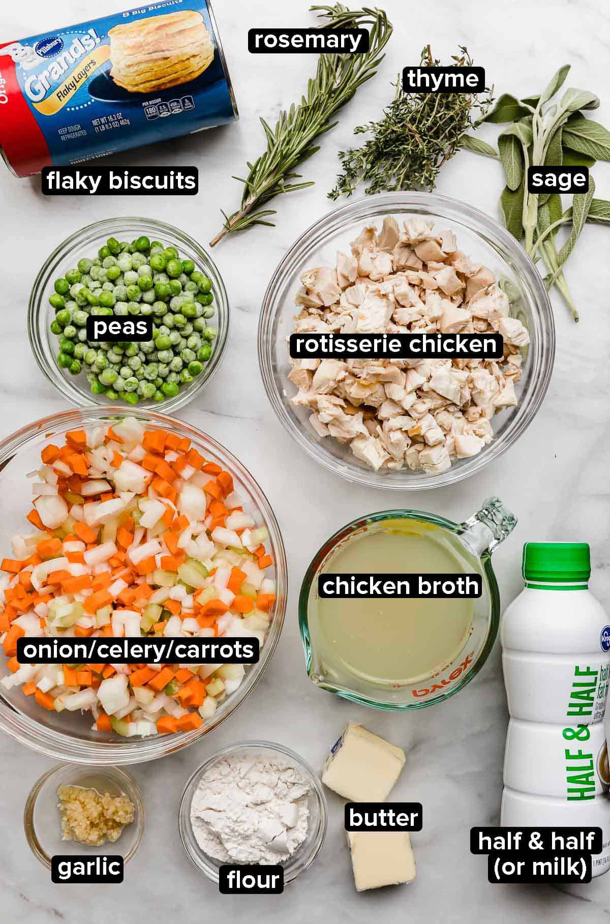 Cast Iron Chicken Pot Pie ingredients on a white marble surface: onion, carrot, celery, rosemary, thyme, sage, butter, chicken broth, flour, peas, chicken, and milk (half and half).