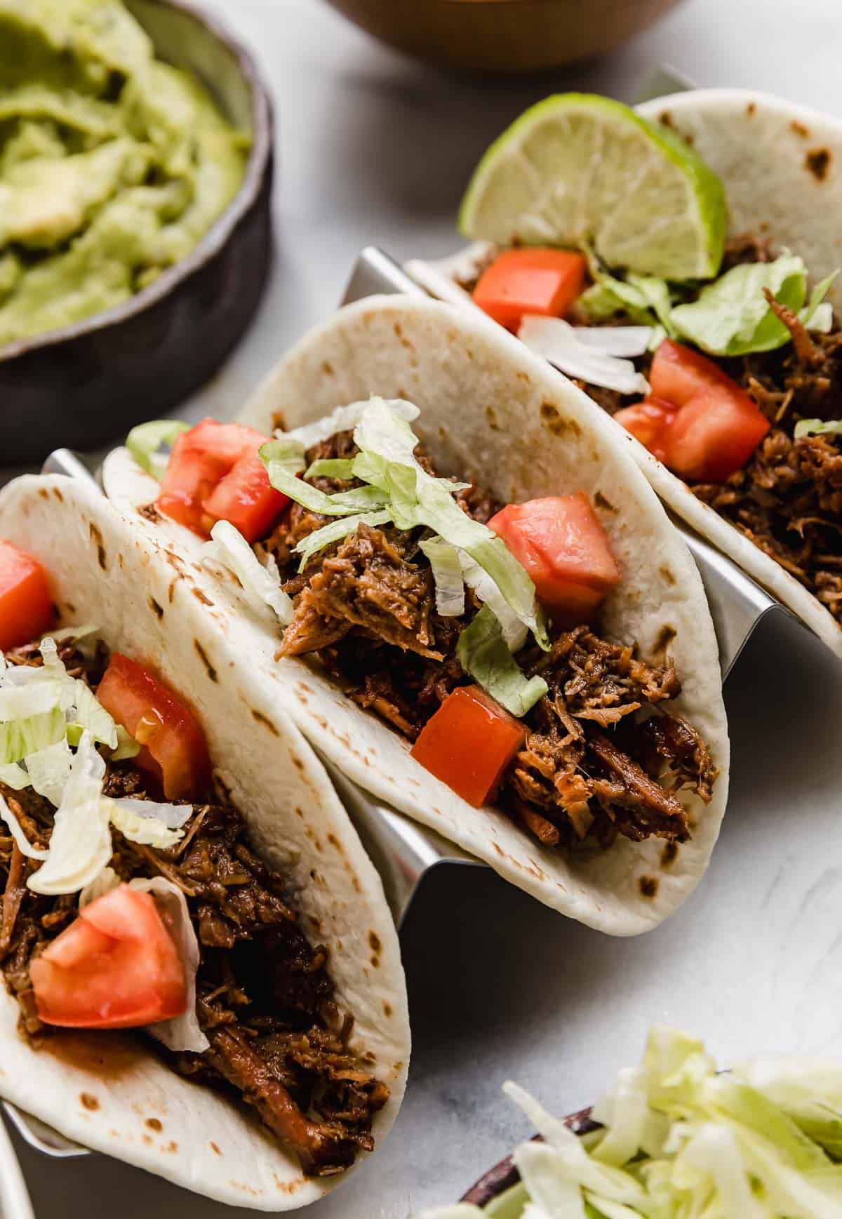 Three shredded beef tacos (made in the crock pot) topped with lettuce, tomato and guacamole.