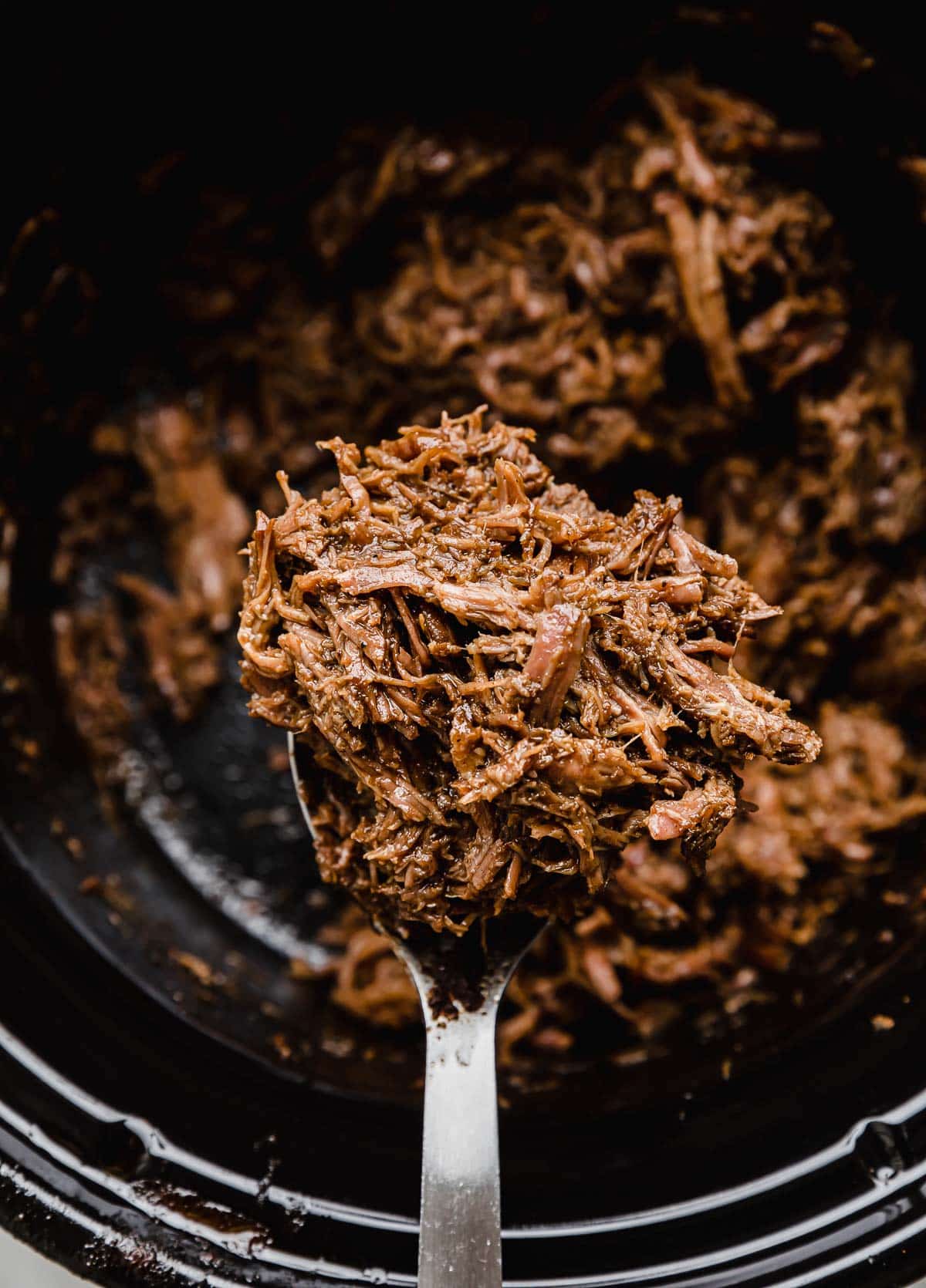 Crock Pot Shredded Beef Taco meat balancing on a spoon over a black crock pot.