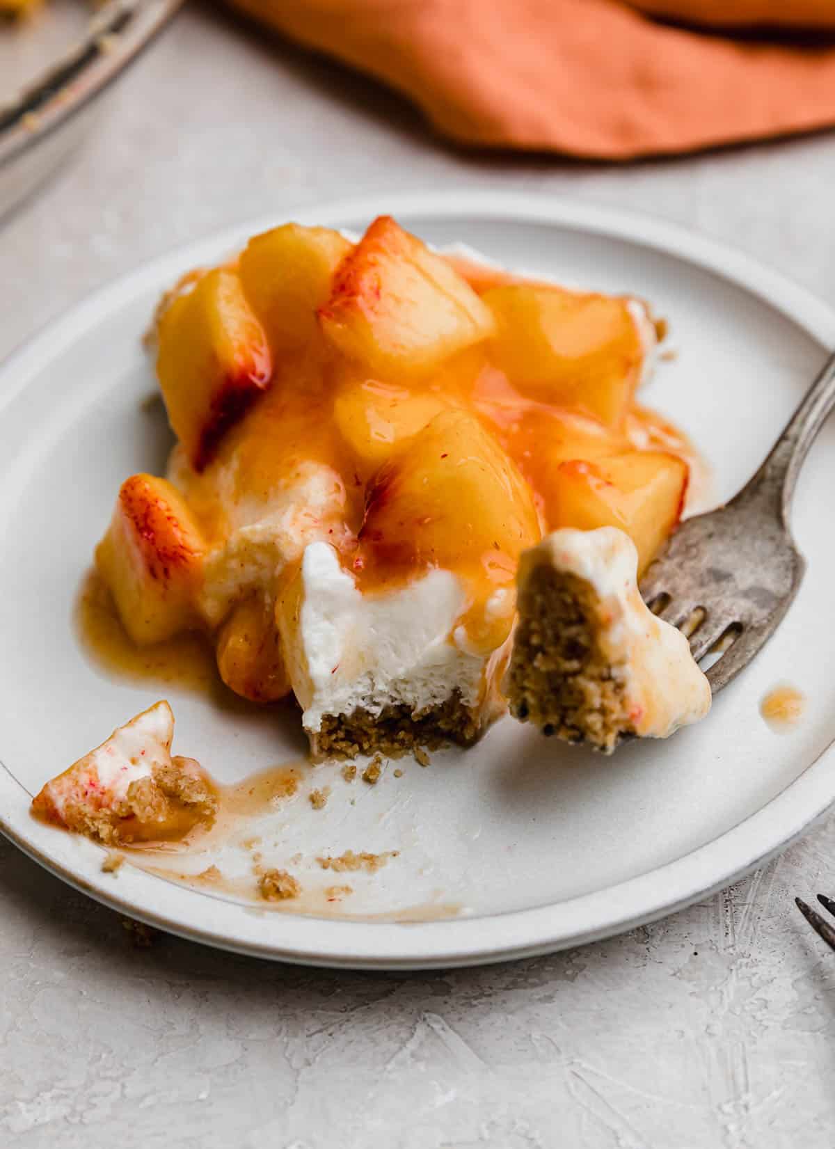 A slice of Peach Cream Pie on a white plate with a fork cutting a bite from the tip of the pie slice.