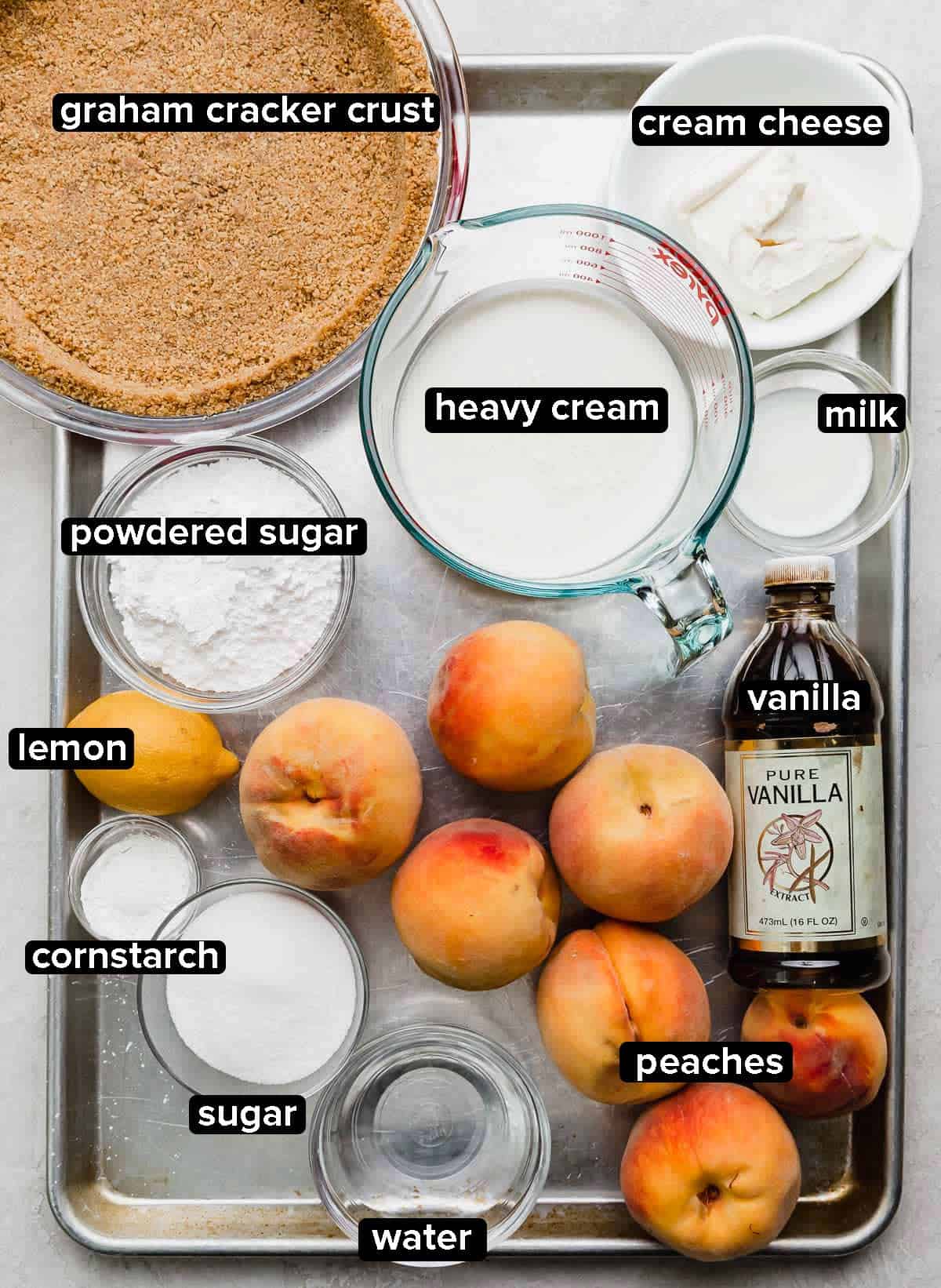 Fresh Peach Cream Pie recipe ingredients on a baking sheet: fresh peaches, graham cracker pie crust, cream cheese, milk, vanilla, cornstarch, lemon, and water.