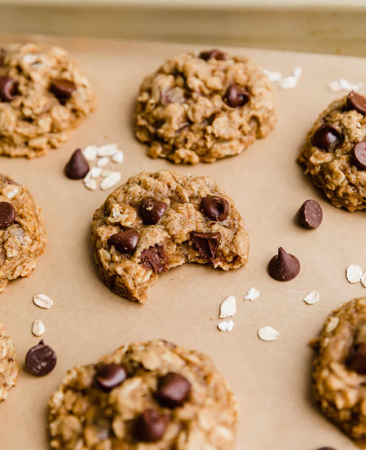 A Chocolate Chip Oatmeal Pumpkin Cookie with a bite taken out of the cookie, on a Kraft parchment lined baking sheet.