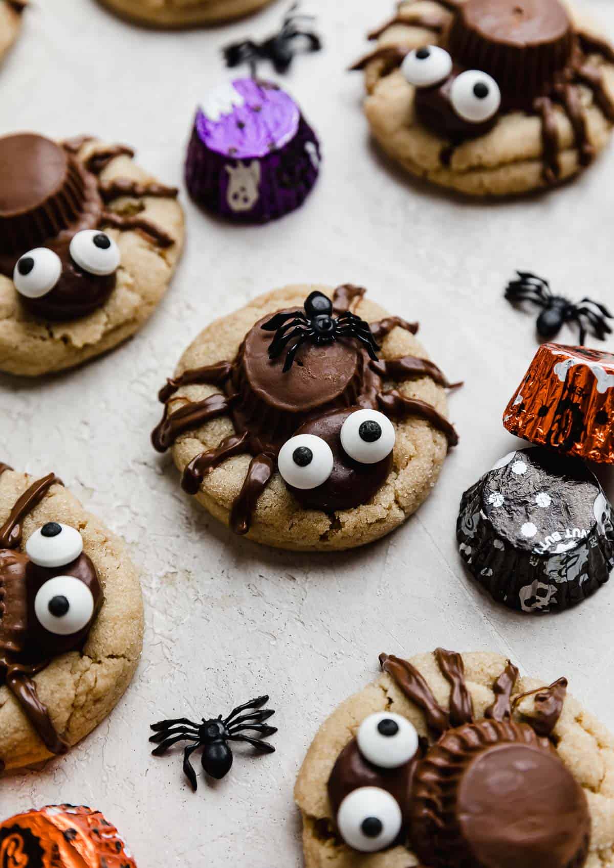 Peanut butter spider cookies made to look like Halloween Spider Cookies with an upside down Reeses peanut butter cup, milk dud, and candy eyes with 8 legs drawn on with melted chocolate.