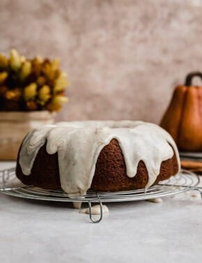 Moist Pumpkin Bundt Cake topped with brown butter glaze with a pumpkin in the background.