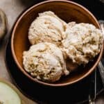 Three scoops of Apple Pie Ice Cream studded with cinnamon apples and cinnamon graham cracker pieces in a brown bowl.