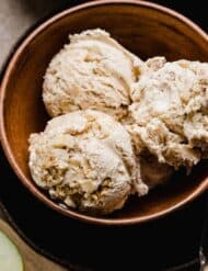 Three scoops of Apple Pie Ice Cream studded with cinnamon apples and cinnamon graham cracker pieces in a brown bowl.