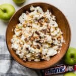 Overhead photo of a salad with snickers and apples in a brown bowl topped with caramel to make the best Apple Snickers Salad recipe.