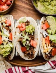 Three flour tortillas filled with Crock Pot Shredded Beef Taco mix, shredded lettuce, guacamole, and tomatoes.