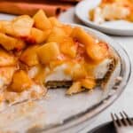 A Peach Cream Pie made with cream cheese base layer on a graham cracker crust and topped with chopped fresh peaches.