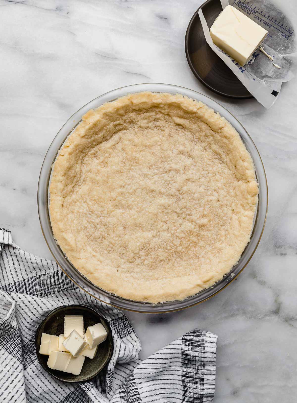 The best Shortbread Pie Crust recipe baked in a 9" pie plate on a white marble surface.