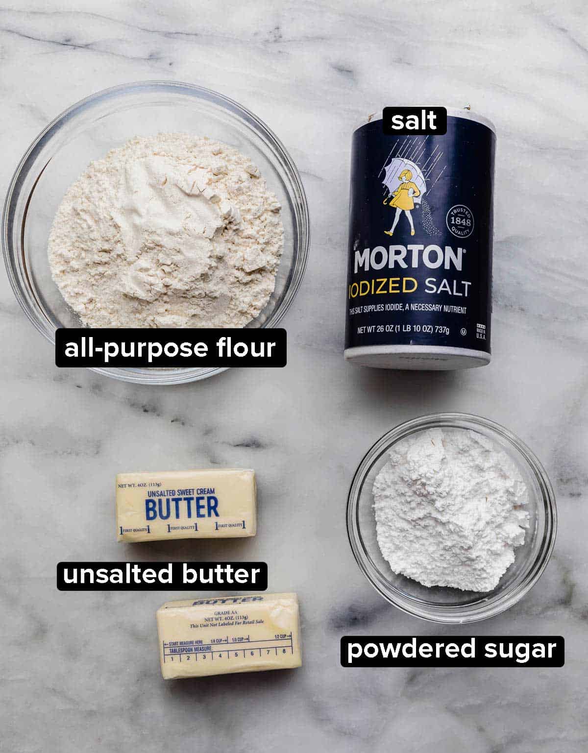 Shortbread Pie Crust ingredients on a marble surface: flour, salt, butter, and powdered sugar.