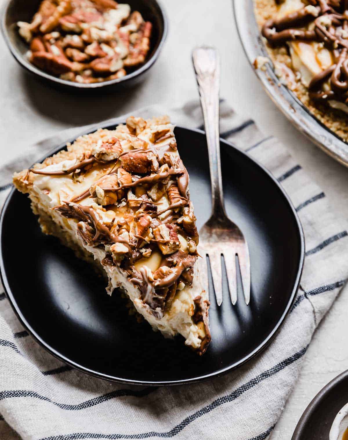 A slice of cream cheese caramel turtle pie on a black plate.