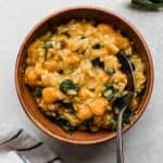 Brown bowl filled with Butternut Squash Orzo pasta with kale and sage brown butter sauce, on a light gray surface.
