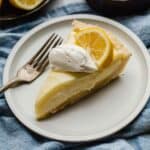 Lemon Sour Cream Pie on a white plate with a dollop of whipped cream and lemon slice on top.