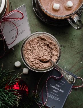 Overhead photo of Homemade Hot Cocoa Mix in a glass mason jar on a dark forest green background.