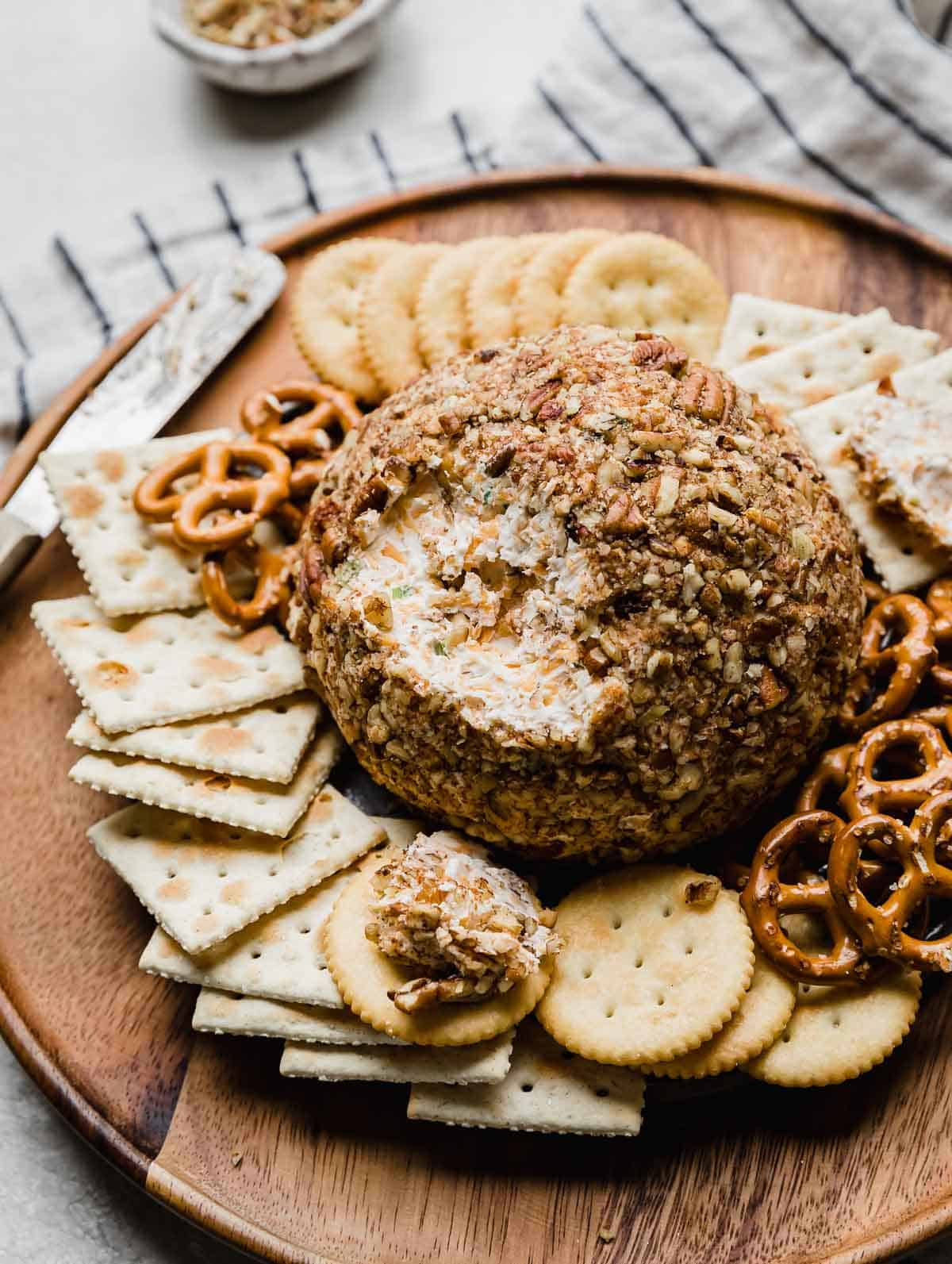 A Christmas Cheese Ball covered with pecans on a brown plate surrounded by crackers.