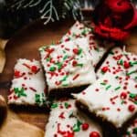 Gingerbread Cookie Bars topped with cream cheese frosting and red and green sprinkles, on a brown plate.