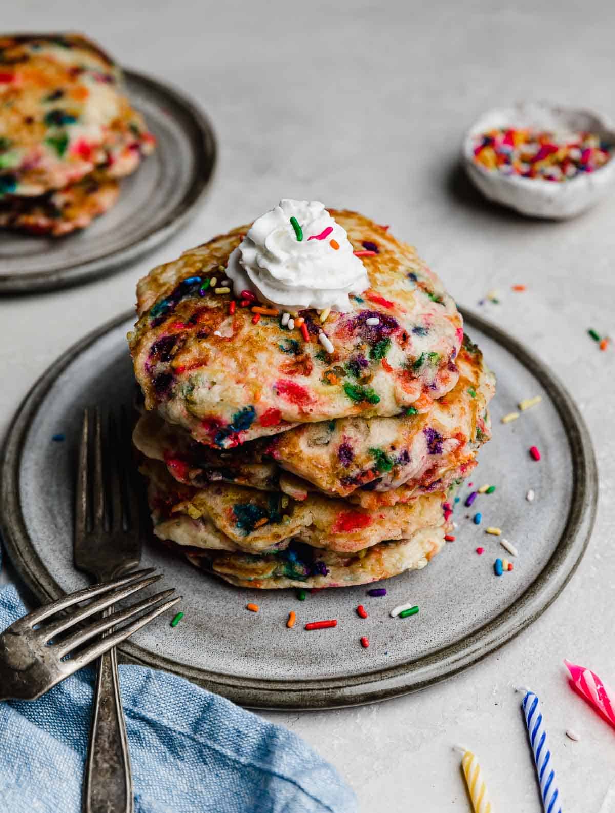 Birthday Cake Pancakes on a gray plate on a light gray background with birthday candles next to the plate. 