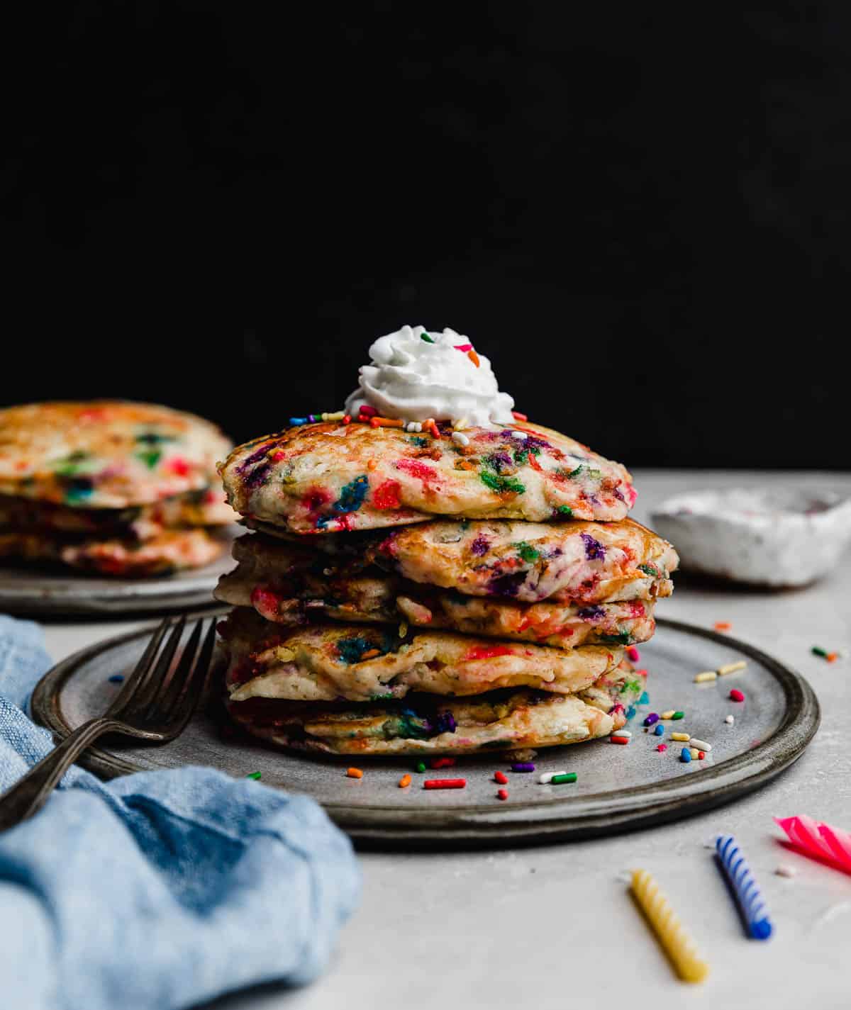 A stack of Birthday Cake Pancakes (funfetti pancakes) on a gray plate against a black background. 