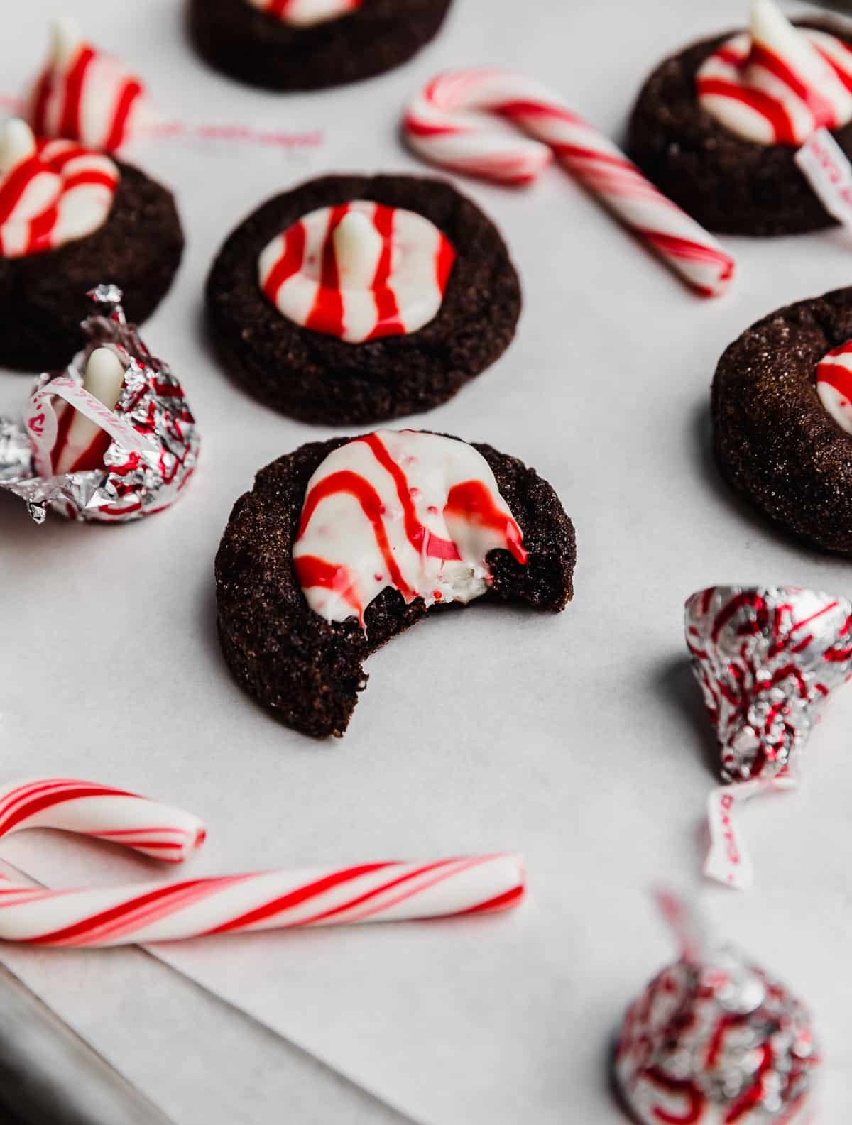 A chocolate peppermint blossom cookie on a white parchment paper with a bite taken out of the cookie.