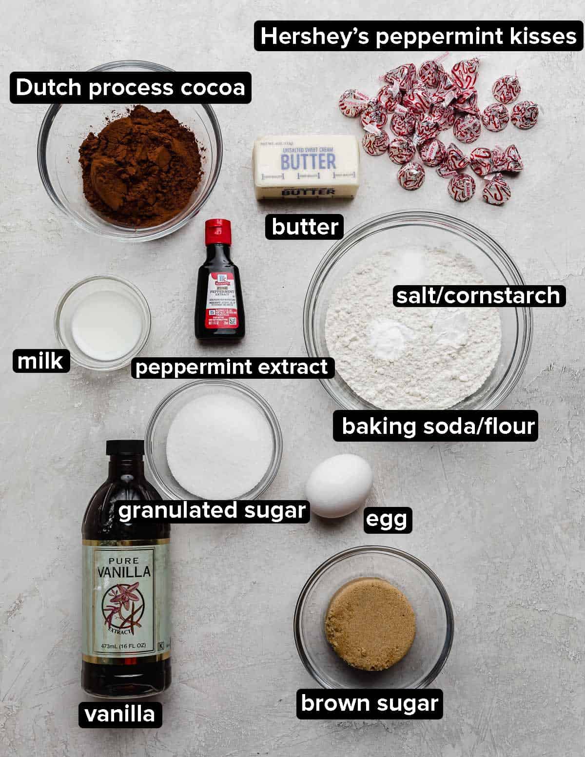 Chocolate Peppermint Blossom cookies ingredients on a light gray background: cocoa, sugars, egg, butter, Hershey's kisses, and peppermint extract.