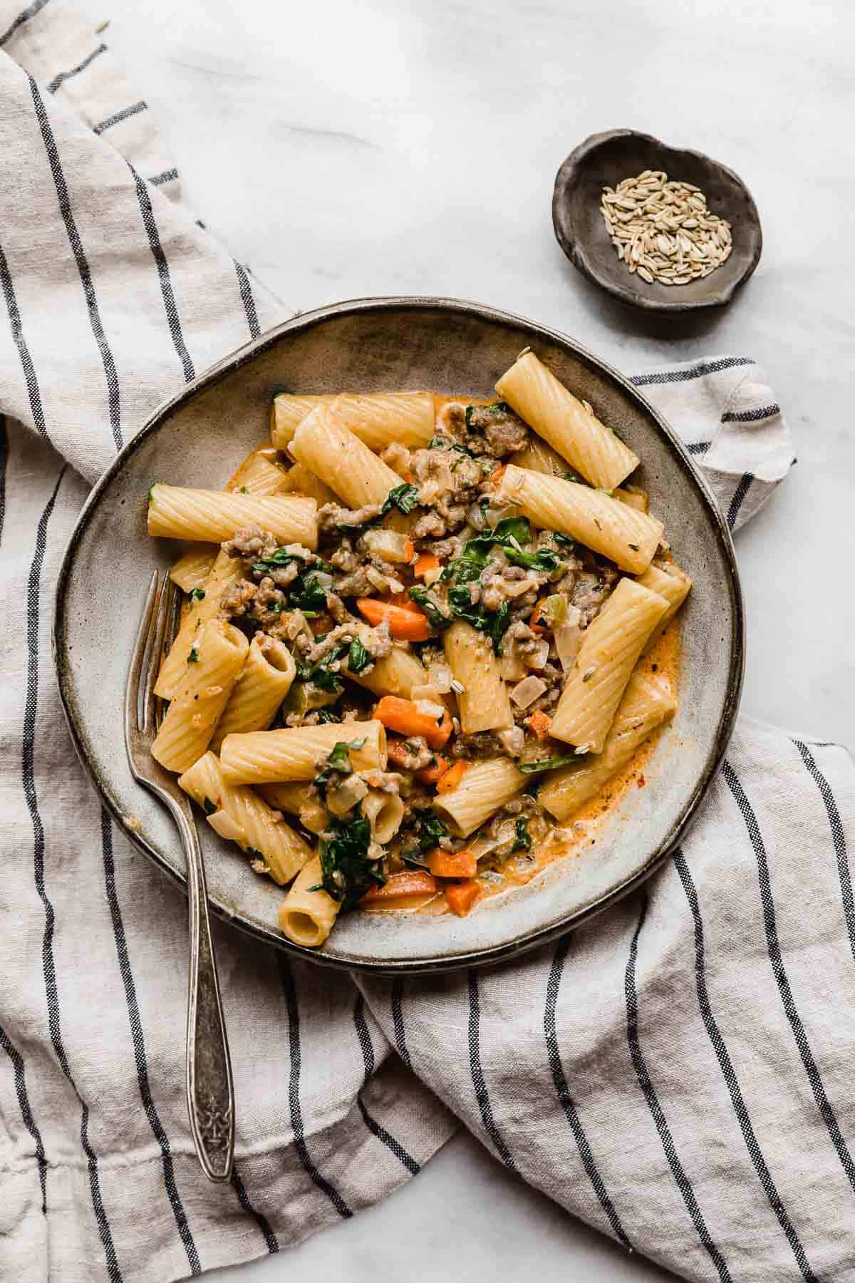 A gray pasta plate topped with the best Sausage and Rigatoni pasta recipe with carrots and spinach.