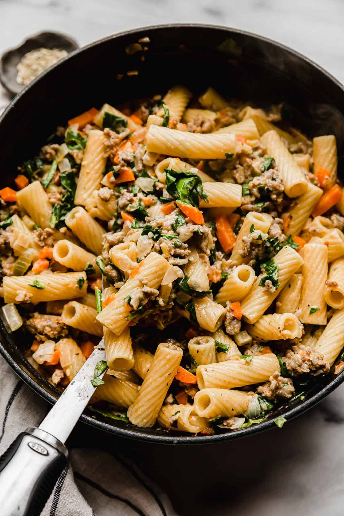 A serving spoon scooping up a portion of homemade Italian Sausage Rigatoni from a large pot.