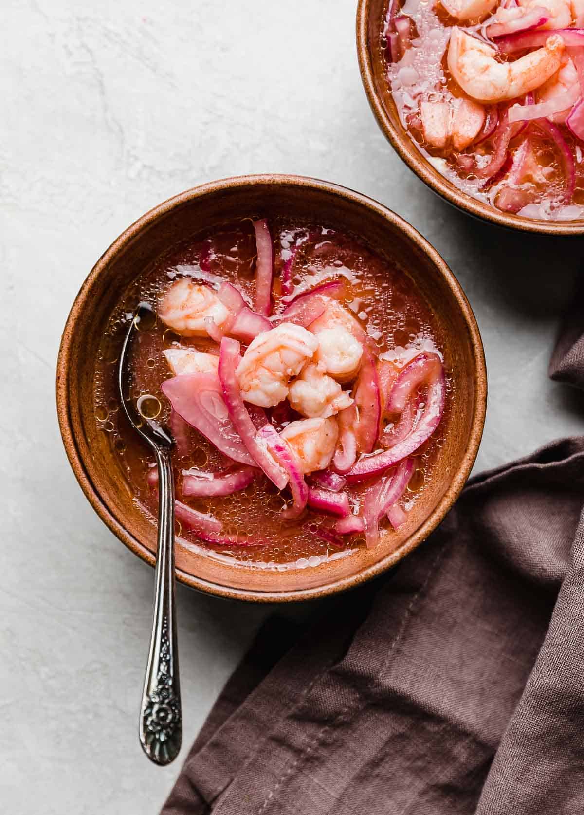 A traditional Shrimp Ceviche recipe in a brown bowl with a deep purple colored napkin to the right side of the bowl.