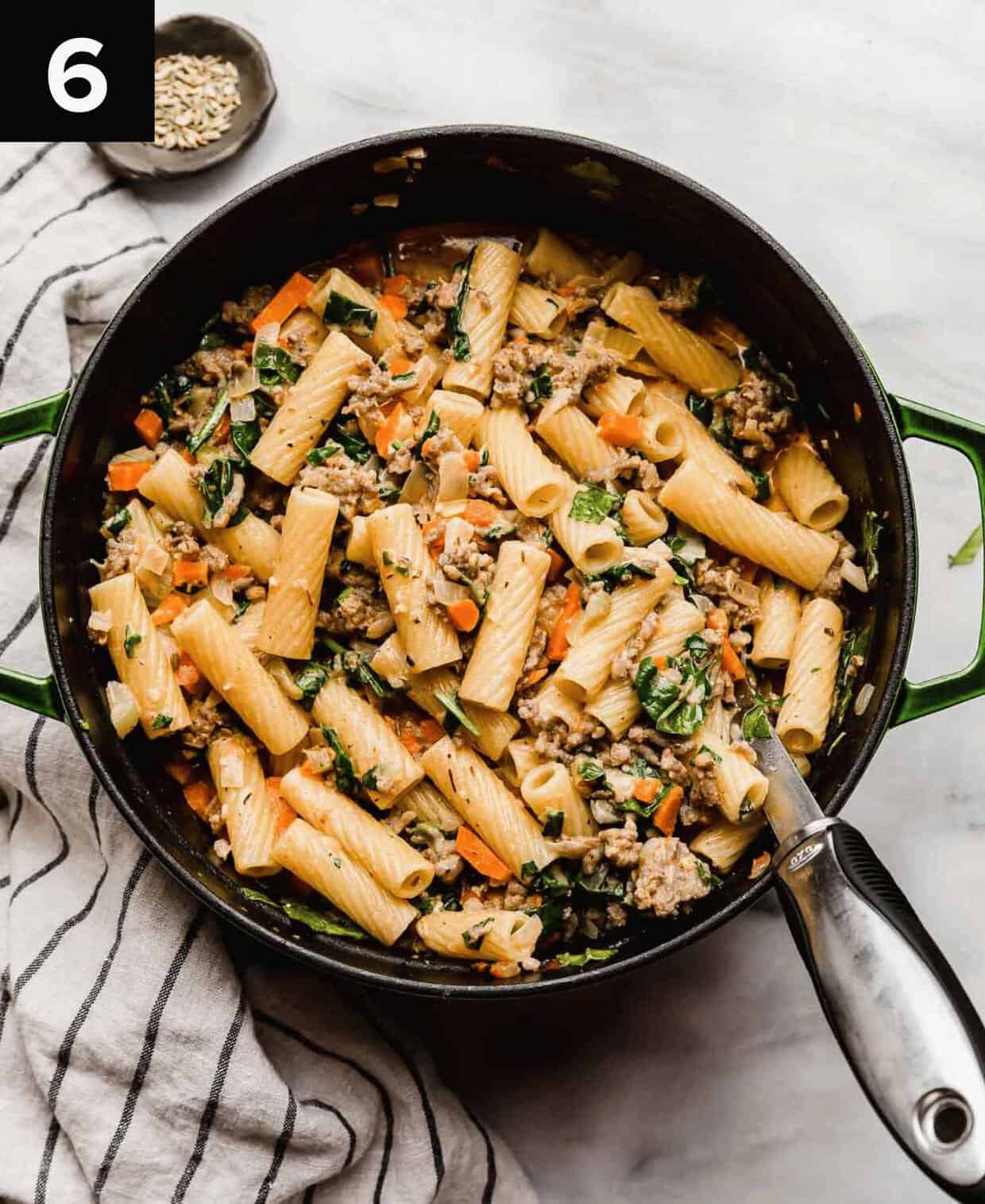 The best Italian Sausage Rigatoni recipe with spices and spinach in a large dutch oven with a large silver serving spoon in the pasta.