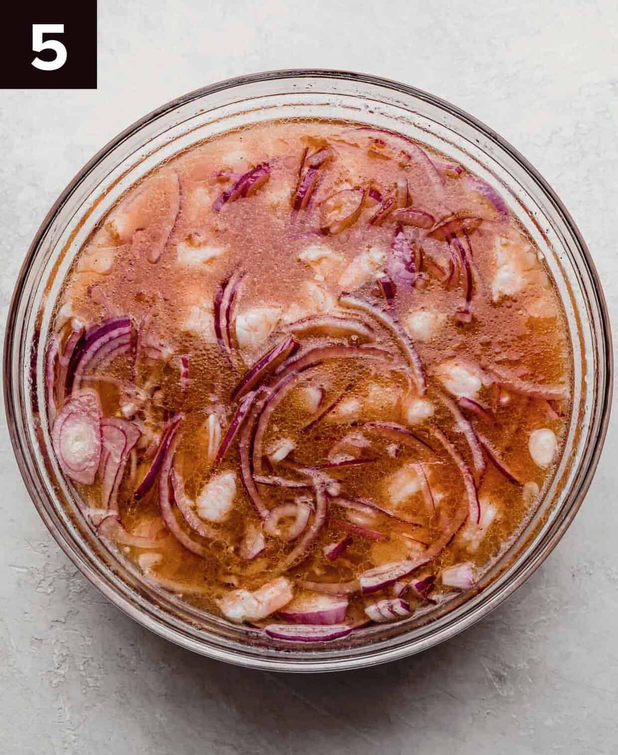 Cooked shrimp, purple onion, and acidic mixture in a glass bowl.