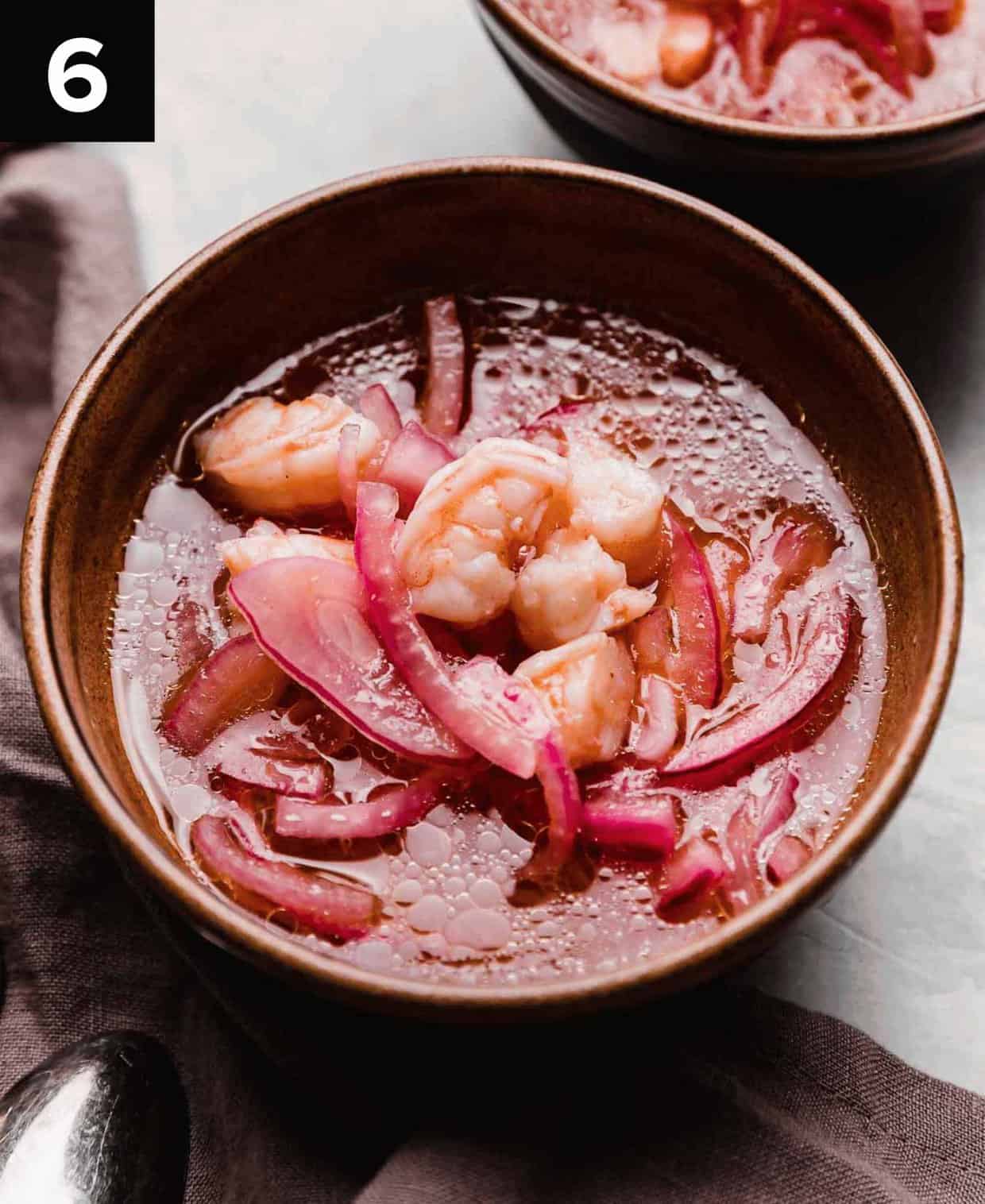 A Shrimp Ceviche soup with purple onions in a brown bowl on a light gray surface.