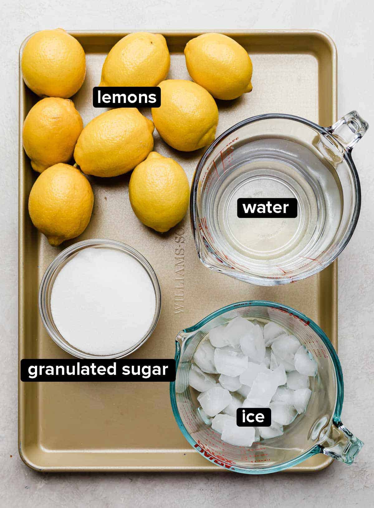 Chick-fil-A Lemonade Recipe ingredients on a gold baking sheet: real lemons, water, sugar, and ice.