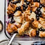 Overhead photo of Blueberry Croissant Breakfast casserole in a glass baking dish on a white surface.