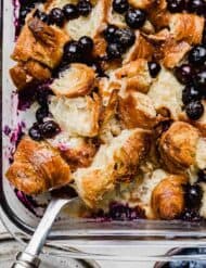 Overhead photo of Blueberry Croissant Breakfast casserole in a glass baking dish on a white surface.