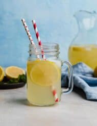 A glass of fresh lemonade in a mason jar cup against a light blue background with two red straws in the cup.
