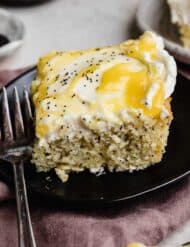 A slice of moist lemon poppy seed sheet cake on a black plate.