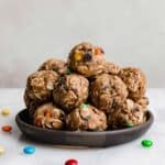 Monster Cookie Protein Balls with protein powder and M&M's on a black plate against a white background.