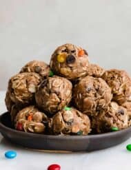 Monster Cookie Protein Balls with protein powder and M&M's on a black plate against a white background.
