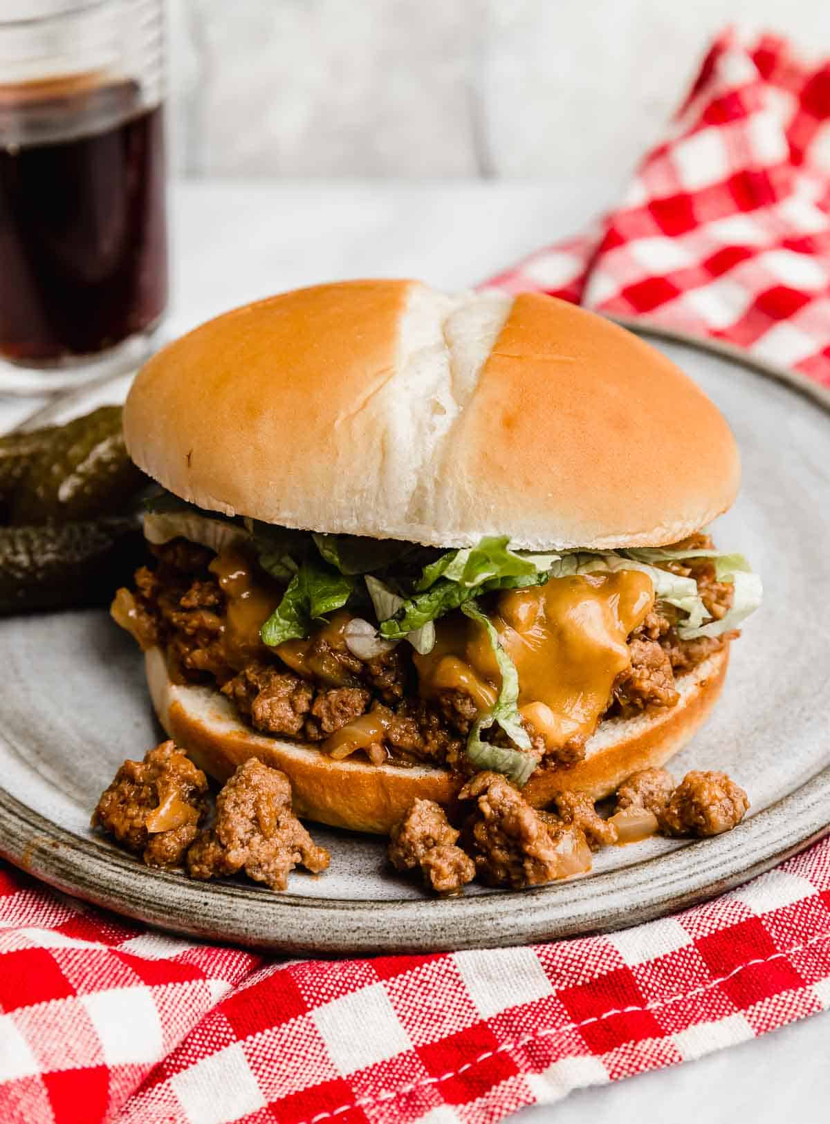 Close up photo of a Cheeseburger Sloppy Joe on a gray plate with meat mixture spilling onto the plate, topped with melty cheese and shredded lettuce.