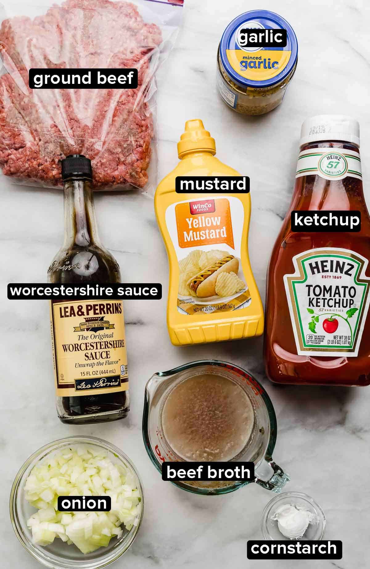 Ingredients used to make the best Cheeseburger Sloppy Joes on a white marbled surface: ground beef, mustard, ketchup, onion, beef broth, garlic, and Worcestershire sauce.