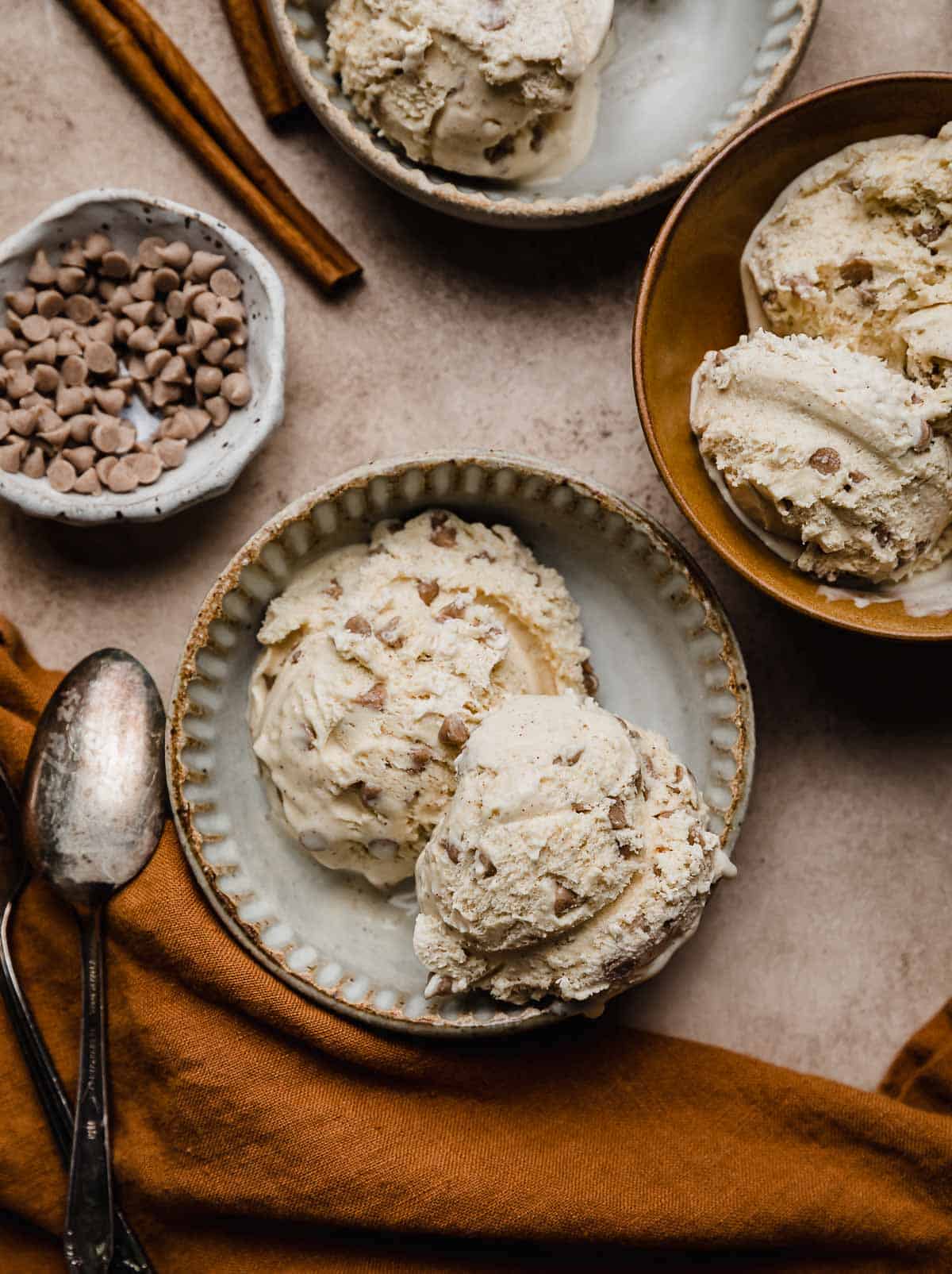 Overhead photo of cinnamon chip ice cream on a brown surface with a burnt orange napkin near the bowl of ice cream.