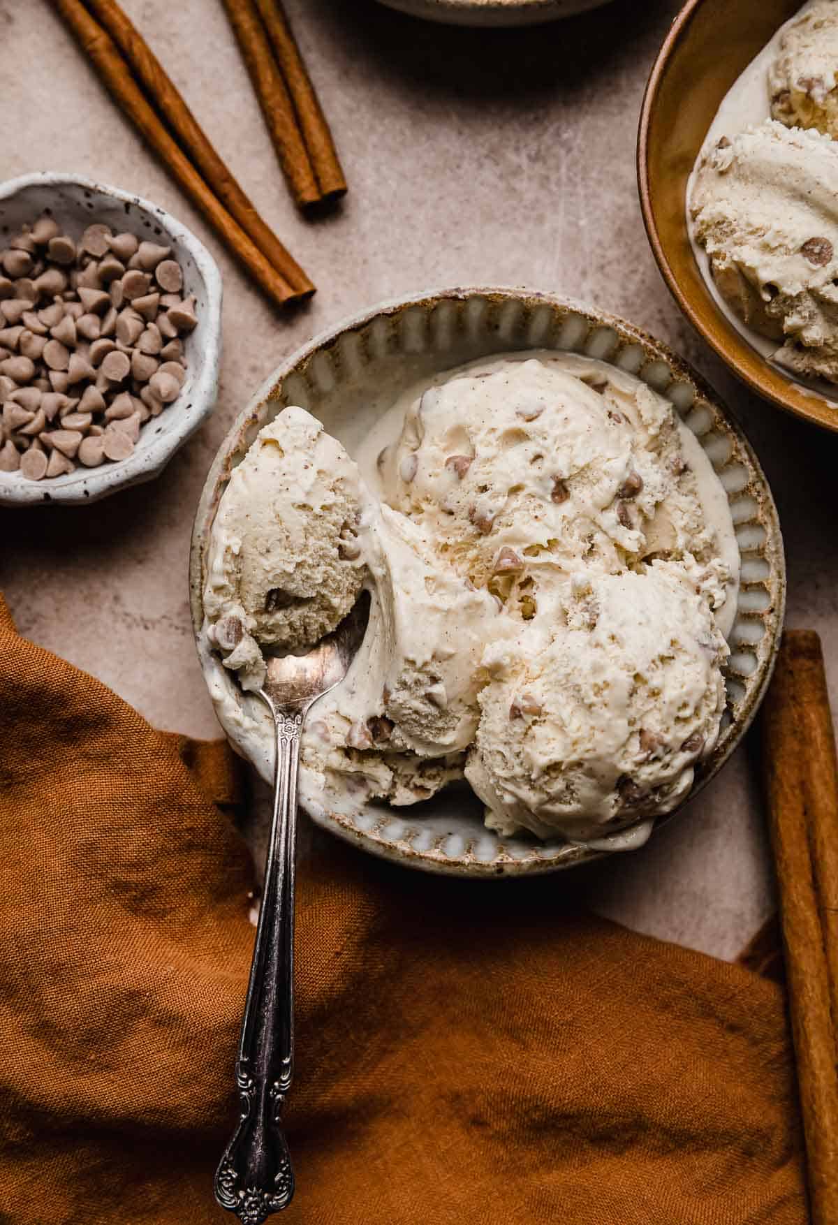 Cinnamon Chip Ice Cream in a pottery bowl on a light brown textured background with a spoon scooping out some of the creamy ice cream.